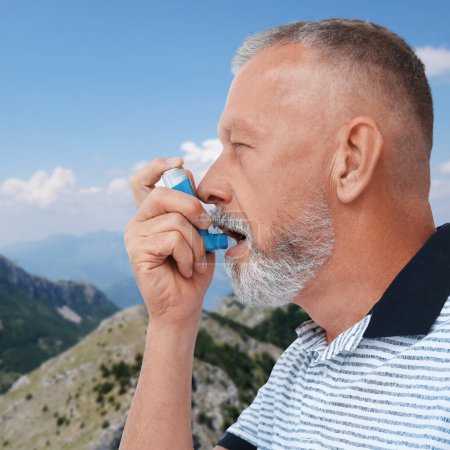 Photo for Mature man using asthma inhaler in mountains. Emergency first aid during outdoor recreation - Royalty Free Image