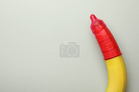 Téléchargez les photos : Banane avec préservatif sur fond gris clair, vue de dessus et espace pour le texte. Sexe sans risque - en image libre de droit