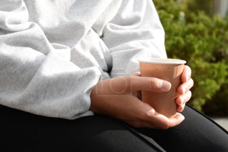 Photo for Woman sitting with cardboard cup of coffee outdoors, closeup - Royalty Free Image