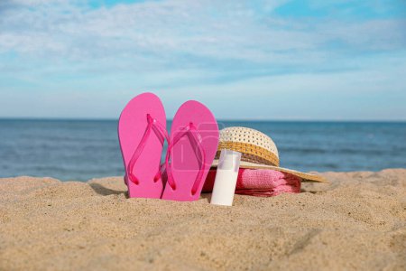 Photo for Beach towel, slippers, sunscreen and straw hat on sand near sea - Royalty Free Image