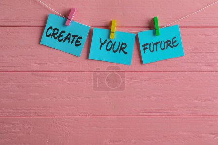 Téléchargez les photos : Notes de papier avec phrase de motivation Créer votre avenir accroché sur un mur en bois rose. Espace pour le texte - en image libre de droit