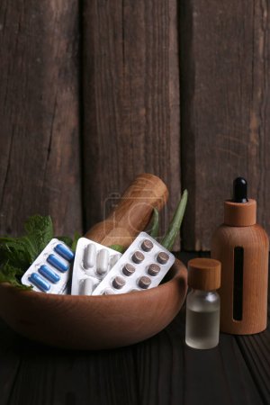 Photo for Mortar with fresh green herbs, extracts and pills on wooden table - Royalty Free Image