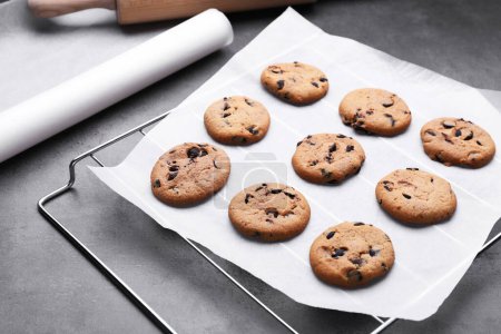 Téléchargez les photos : Rouleau de papier sulfurisé et support de refroidissement avec biscuits savoureux sur table gris foncé - en image libre de droit