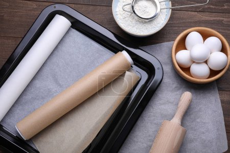 Téléchargez les photos : Plaque de cuisson avec rouleaux de papier sulfurisé, différents ingrédients et outils de cuisine sur table en bois, pose plate - en image libre de droit