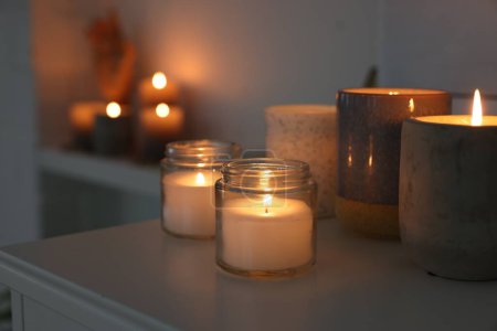 Photo for Burning wax candles on white table in room, space for text - Royalty Free Image