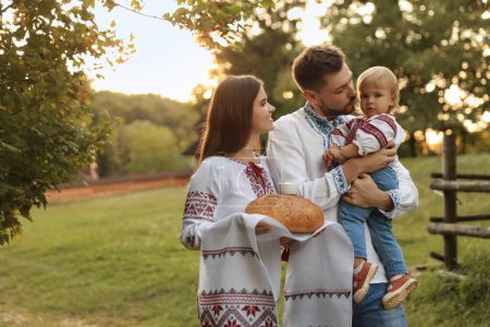 Foto de Feliz linda familia en camisas ucranianas bordadas con pan korovai en el día soleado. Espacio para texto - Imagen libre de derechos