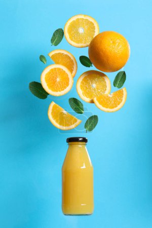 Photo for Tasty ripe oranges and green leaves over glass bottle on light blue background - Royalty Free Image