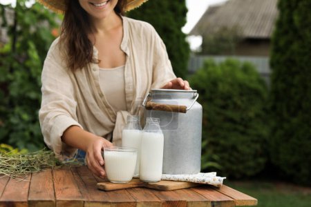 Foto de Mujer sonriente tomando vidrio con leche fresca en la mesa de madera al aire libre, primer plano - Imagen libre de derechos