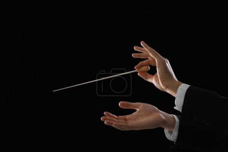 Professional conductor with baton on black background, closeup. Space for text