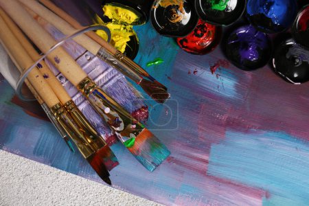Foto de Lienzo con pintura abstracta de colores y diferentes pinceles, vista superior - Imagen libre de derechos