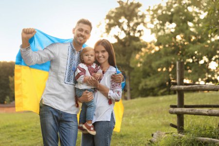 Happy cute family in embroidered national shirts with Ukrainian flag on sunny day. Space for text