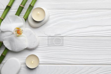 Photo for Bamboo stems, orchid, spa stones and burning candles on white wooden table, flat lay. Space for text - Royalty Free Image