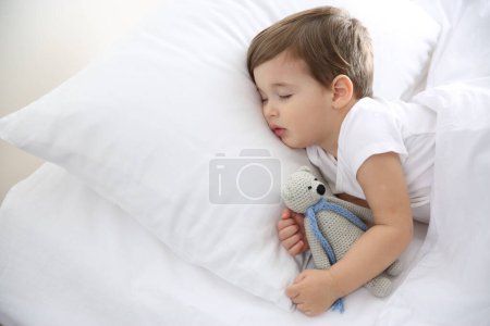 Téléchargez les photos : Mignon petit bébé dormant avec jouet à la maison. Au lit. - en image libre de droit
