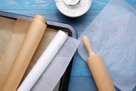 Téléchargez les photos : Papier sulfurisé, plaque à pâtisserie, rouleau à pâtisserie et farine sur table en bois bleu clair, plat - en image libre de droit
