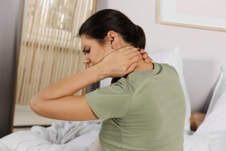 Young woman suffering from neck pain on bed in bedroom