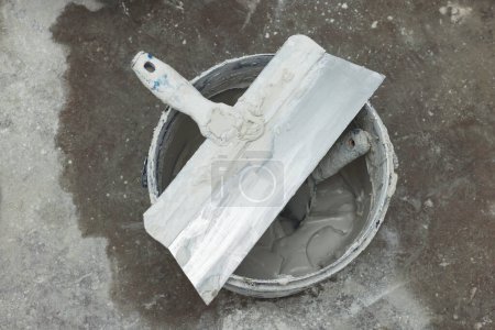 Foto de Cubo con yeso y cuchillos de masilla en piso de hormigón, vista superior - Imagen libre de derechos