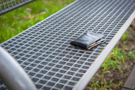 Black wallet on metal bench outdoors, space for text. Lost and found