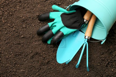 Photo for Overturned bucket with gardening tools and gloves on fresh soil, flat lay. Space for text - Royalty Free Image