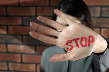 Foto de Concepto de violencia doméstica. Mujer infeliz escondiendo su cara, concéntrate en la mano con la palabra escrita Stop - Imagen libre de derechos