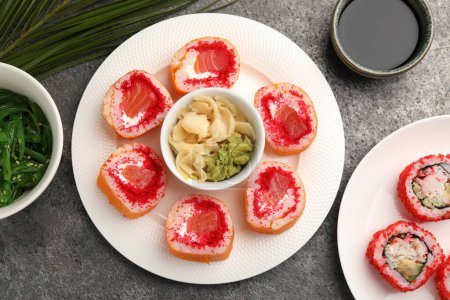 Foto de Deliciosos rollos de sushi con wasabi, jengibre, chuka y salsa de soja sobre una mesa de textura gris, puesta plana - Imagen libre de derechos