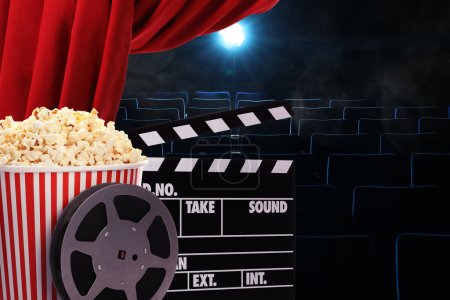 Téléchargez les photos : Popcorn savoureux, bobine de film et clapperboard sous le rideau principal rouge au cinéma, espace pour le texte - en image libre de droit
