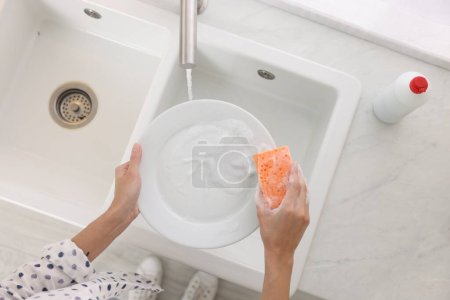 Woman washing plate above sink in modern kitchen, top view