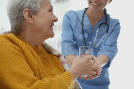 Téléchargez les photos : Travailleur soignant donnant de l'eau à une femme âgée en hospice gériatrique, gros plan - en image libre de droit