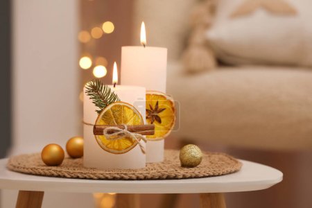 Téléchargez les photos : Belles bougies brûlantes décorées de tranches d'orange sèches et de bâtonnets de cannelle sur une table blanche à l'intérieur. Ambiance Noël - en image libre de droit