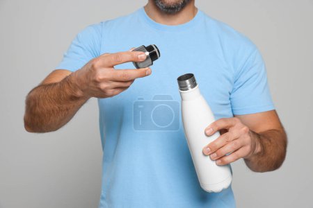 Téléchargez les photos : Homme ouvrant thermo bouteille sur fond gris clair, gros plan - en image libre de droit