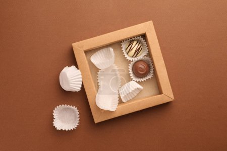 Teilweise leere Schachtel Schokoladenbonbons auf braunem Hintergrund, Ansicht von oben
