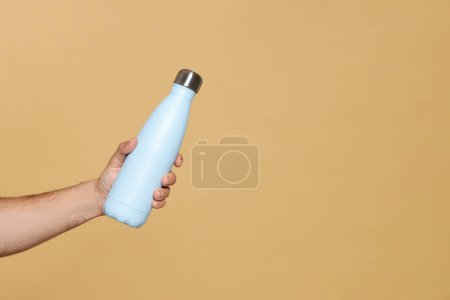 Téléchargez les photos : Homme tenant une bouteille thermo sur fond beige, gros plan. Espace pour le texte - en image libre de droit