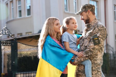 Téléchargez les photos : Soldat en uniforme militaire réuni avec sa famille et drapeau ukrainien à l'extérieur - en image libre de droit