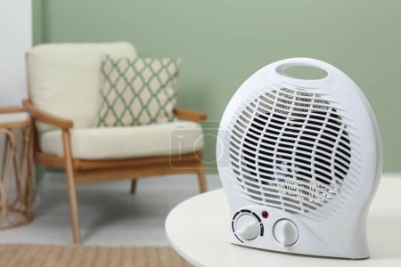 Electric fan heater on white table indoors. Space for text