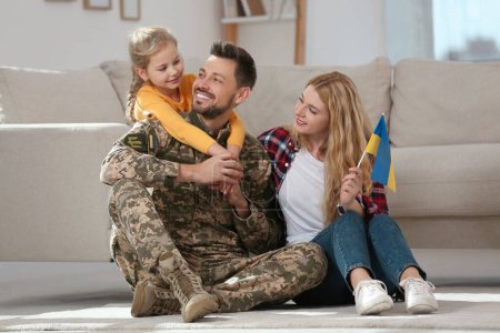 Soldado en uniforme militar se reunió con su familia y la bandera de Ucrania en el suelo en casa