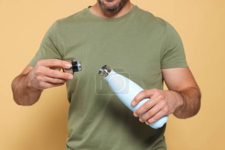 Téléchargez les photos : Homme ouvrant thermo bouteille sur fond beige, gros plan - en image libre de droit
