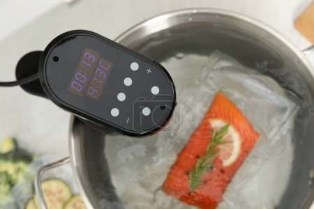 Photo for Sous vide cooker and vacuum packed salmon in pot on white table, closeup. Thermal immersion circulator - Royalty Free Image