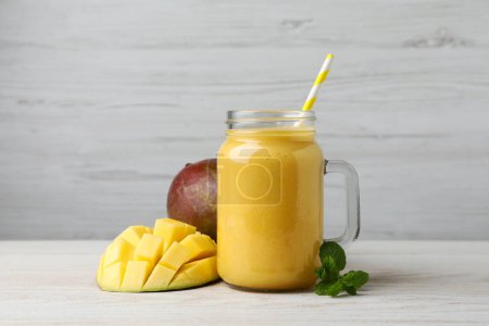 Einmachglas mit leckerem Frucht-Smoothie und frischer Mango auf weißem Holztisch