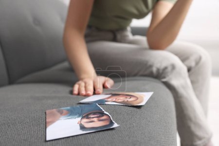Woman sitting near torn photo on sofa indoors, focus on picture. Divorce concept