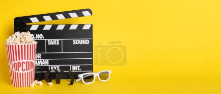 Photo for Delicious popcorn, glasses, tape and clapperboard on yellow background, space for text. Banner design - Royalty Free Image