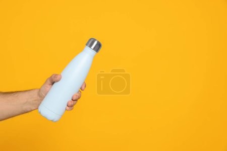 Téléchargez les photos : Homme tenant une bouteille de thermo sur fond orange, gros plan. Espace pour le texte - en image libre de droit