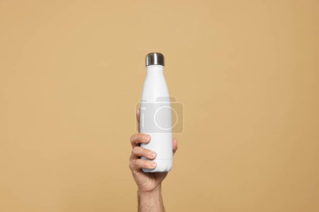 Téléchargez les photos : Homme tenant une bouteille thermo sur fond beige, gros plan - en image libre de droit
