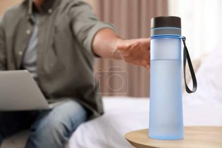 Téléchargez les photos : Homme prenant bouteille d'eau en plastique transparent tout en travaillant sur ordinateur portable à l'intérieur, gros plan - en image libre de droit