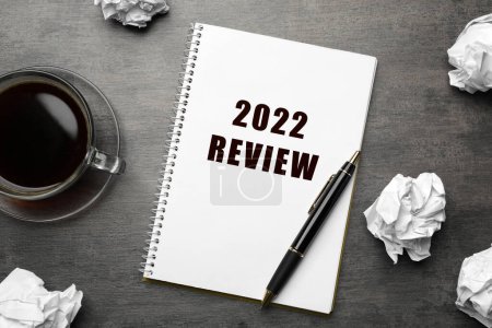 Foto de Texto 2022 Revisión escrita en cuaderno, pluma, taza de café y bolas de papel arrugado en la mesa gris, la puesta plana - Imagen libre de derechos