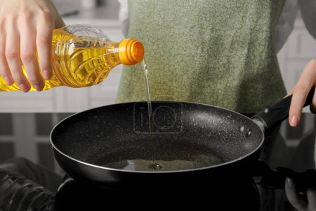 Foto de Mujer vertiendo aceite de cocina de la botella en la sartén en la estufa, primer plano - Imagen libre de derechos