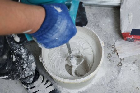 Téléchargez les photos : Travailleur professionnel mélangeant du plâtre dans un seau à l'intérieur, gros plan - en image libre de droit