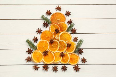 Téléchargez les photos : Composition plate avec des tranches d'orange sèches, des branches de sapin et des étoiles d'anis disposées en forme d'arbre de Noël sur une table en bois blanc - en image libre de droit
