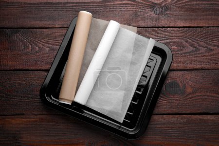 Téléchargez les photos : Plaque de cuisson avec rouleaux de papier parchemin sur table en bois, vue sur le dessus - en image libre de droit