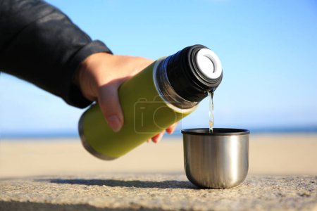 Photo for Woman pouring hot drink from yellow thermos into cap on stone surface outdoors, closeup - Royalty Free Image