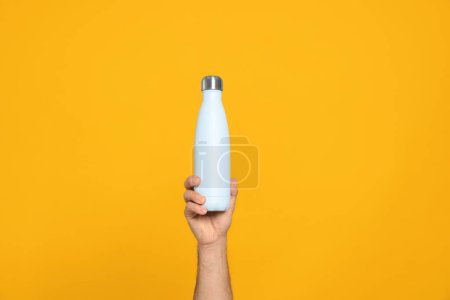 Téléchargez les photos : Homme tenant une bouteille thermo sur fond orange, gros plan - en image libre de droit
