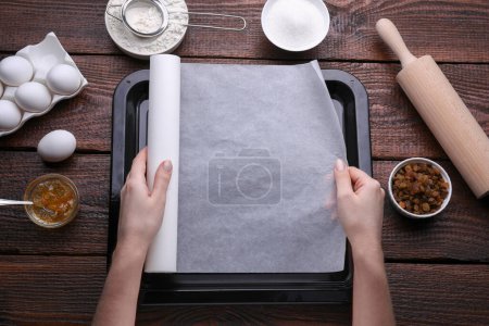 Téléchargez les photos : Femme mettant du papier parchemin dans une casserole à table en bois, vue sur le dessus - en image libre de droit